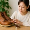 日本人女性がテーブルの上でレッドウィングのブーツを丁寧に手入れしながら経年変化した革の状態を確認している様子
