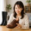 明るい室内で、日本人女性がブラウンレザーのブーツに木製シューキーパーを差し込みながらチェックしている様子を写した写真。後方には黒のロングブーツと観葉植物が置かれている。